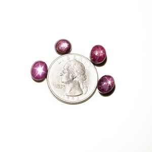 May include: Four pink star ruby cabochons, each about the size of a US quarter, on a white background.