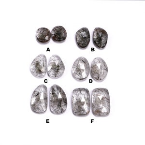 May include: Six pairs of clear quartz gemstones with black inclusions. The gemstones are faceted and have a variety of shapes, including oval, pear, and rectangular.