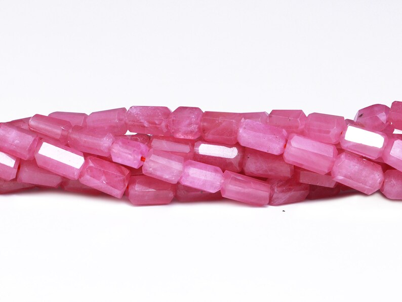 May include: A strand of pink gemstone beads, each bead is faceted and has a rectangular shape.