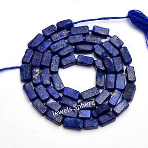 May include: A necklace of rectangular, deep blue lapis lazuli beads with gold flecks. The beads are strung on a blue cord, and the text "Jewels Sphere" is visible. Suitable for crafting necklaces and bracelets.