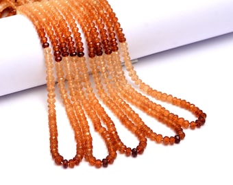 May include: A strand of faceted gemstone beads in shades of orange and brown. The beads are graduated in size, with the larger beads at the bottom of the strand. The beads are strung on a clear thread.