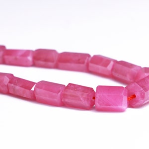 May include: A strand of pink gemstone beads, each bead is faceted and has a rectangular shape.