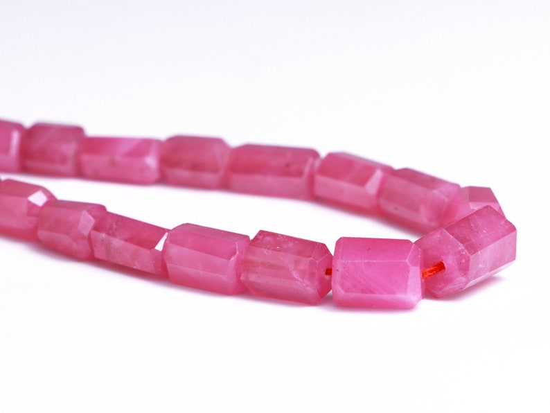 May include: A strand of pink gemstone beads, each bead is faceted and has a rectangular shape.