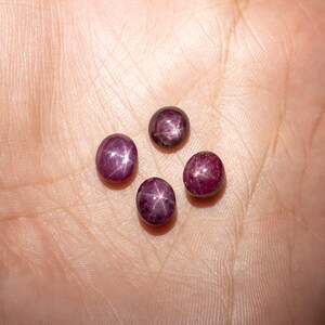 May include: Four round, dark red gemstones with a star-shaped pattern inside. The gemstones are on a light brown surface.