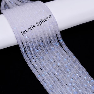 May include: A strand of white moonstone beads, with a slight iridescent shimmer. The beads are faceted and have a slightly irregular shape. The strand is coiled on a white surface with the text "Jewels Sphere" printed on it.