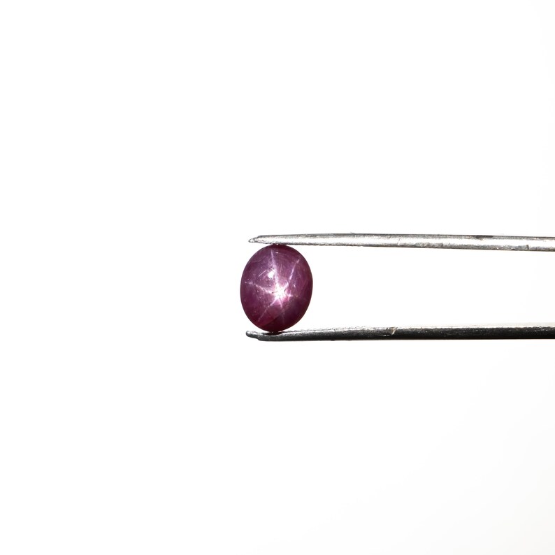May include: A close-up of a deep pink star ruby gemstone held in tweezers. The ruby is round and has a star-shaped pattern.