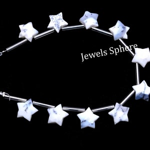 May include: A strand of white star-shaped beads with blue and gray marbling. The beads are strung on silver wire and are separated by silver spacers. The text "Jewels Sphere" is visible in the image.