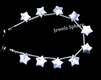 May include: A strand of white star-shaped beads with blue and grey marbling. The beads are strung on silver wire and are separated by silver spacers. The text "Jewels Sphere" is visible in the image.