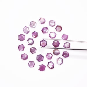 Könnte beinhalten: Eine Sammlung von 20 losen, sechseckigen Steinen aus violettem Edelstein. Die Steine sind in einem Kreis angeordnet, wobei eine Pinzette zwei Steine in der Mitte hält.