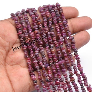 May include: A strand of pink ruby gemstone chips, approximately 4mm in size, strung on a clear thread. The chips are irregular in shape and have a natural, rough texture. The strand is approximately 16 inches long.