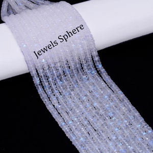 May include: A strand of white moonstone beads, with a slight iridescent shimmer. The beads are faceted and have a slightly irregular shape. The strand is coiled on a white surface with the text "Jewels Sphere" printed on it.