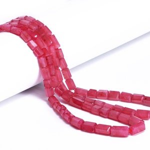 May include: A strand of pink gemstone beads, each bead is rectangular and faceted. The beads are strung on a clear thread and are arranged in a loose, flowing pattern.