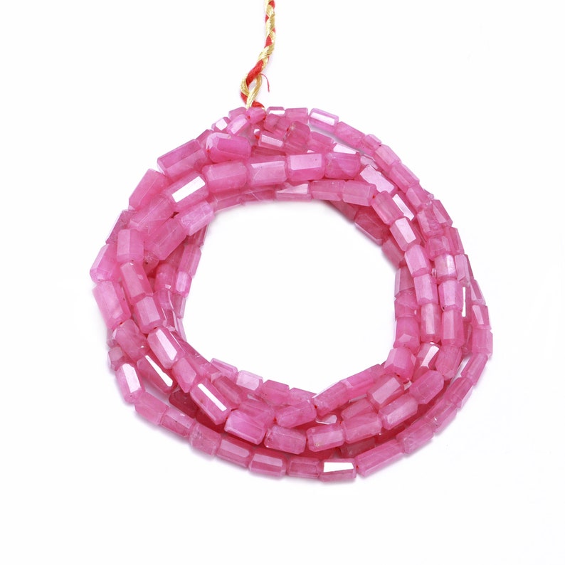 May include: A strand of pink gemstone beads, each bead is faceted and rectangular in shape. The beads are strung on a gold thread.