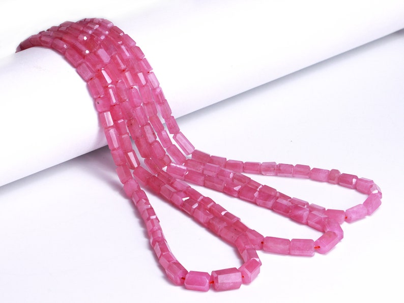 May include: A strand of pink gemstone beads, each bead is rectangular and faceted. The beads are strung on a clear thread and are arranged in a loose, flowing pattern.