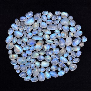 May include: A collection of iridescent moonstone cabochons in various sizes and shapes. The stones are a milky white color with a blue sheen.