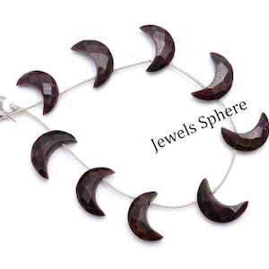 May include: A strand of dark red gemstone crescent moon beads on a silver chain. The beads are faceted and have a shiny finish. The chain has a tassel on one end. The image includes the text "Jewels Sphere".