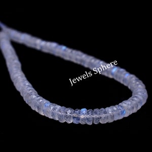 May include: A strand of white moonstone beads with a slight iridescent shimmer. The beads are faceted and have a slightly irregular shape. The strand is displayed on a black background. Jewels Sphere is printed on the image.