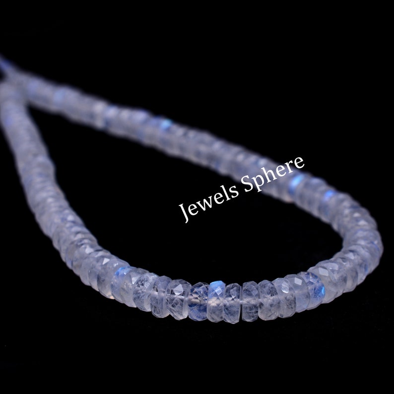 May include: A strand of white moonstone beads with a slight iridescent shimmer. The beads are faceted and have a slightly irregular shape. The strand is displayed on a black background. Jewels Sphere is printed on the image.