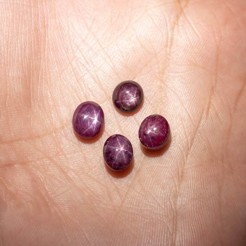 May include: Four round, dark red gemstones with a star-shaped pattern inside. The gemstones are on a light brown surface.