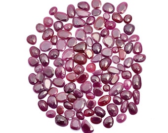 May include: A large collection of loose, faceted ruby gemstones in various shades of pink and red. The stones are scattered on a white background.