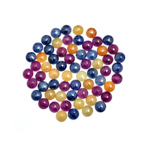 May include: A collection of round, faceted gemstones in shades of blue, yellow, and pink. The gemstones are arranged in a circular pattern on a white background.