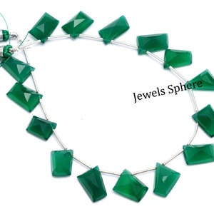 May include: A strand of green gemstone beads, each bead is a rectangular faceted shape. The beads are strung on a silver chain with silver clasps. The strand is displayed on a white background with two green tassels.