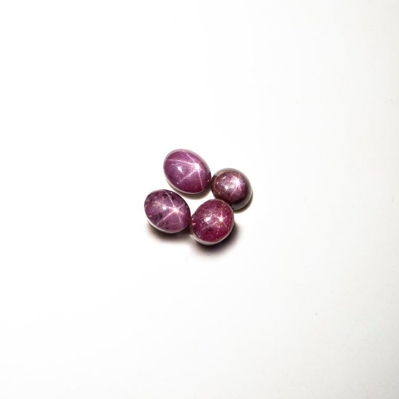 May include: Four pink star ruby gemstones on a white background.