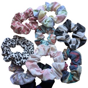 Könnte beinhalten: Eine Sammlung von neun bunten Haargummis aus Stoffresten. Die Haargummis haben verschiedene Muster, darunter Blumen, Leopardenmuster, Batik und Karos.