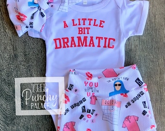 May include: A white baby onesie with the text "A Little Bit Dramatic" in red. A white headband with pink lips and a calendar print. White shorts with a pink and blue print featuring the text "You Can't Sit With Us" and "So Fetch".