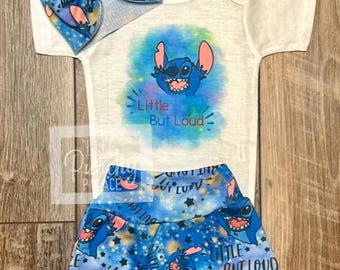 May include: A baby outfit set featuring a white onesie with a blue cartoon character graphic and the text "Little But Loud." The set includes matching blue shorts and a bow headband, all with the same character print.