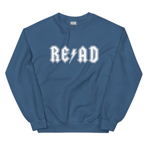 Puede incluir: Una sudadera azul con un gr&aacute;fico blanco que dice "RE&emsp;AD" en una fuente de rock and roll.