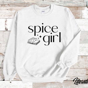 May include: White sweatshirt with the words "spice girl" in a black, elegant font, with a small book graphic and stars. The word "Literaturally" is printed in a script font at the bottom right corner.