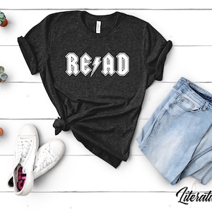May include: A black t-shirt with a white graphic that says "READ" in a rock and roll font with a lightning bolt.