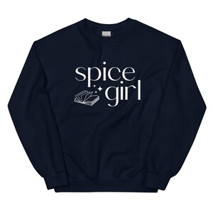 May include: A navy blue sweatshirt with the words "spice girl" in white script. A small open book graphic is below the words. The sweatshirt is a crew neck style.