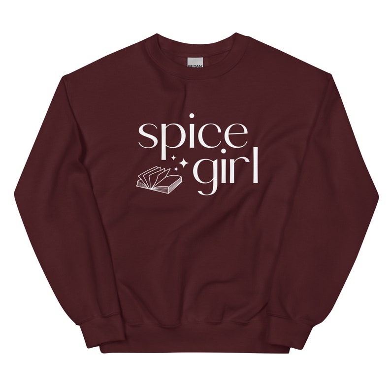 May include: A maroon sweatshirt with the words "spice girl" in white script. A small open book graphic and stars are next to the word "girl". The sweatshirt is a solid color and has a crew neck.