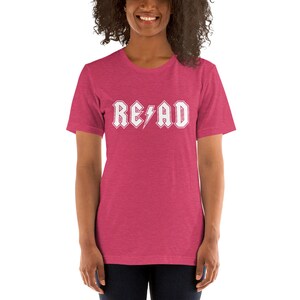 May include: A pink heather short-sleeved t-shirt with a white graphic that says "READ" in a rock and roll font with a lightning bolt.