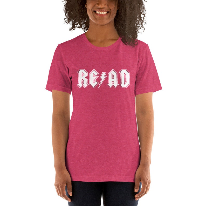 May include: A pink heather short-sleeved t-shirt with a white graphic that says "READ" in a rock and roll font with a lightning bolt.