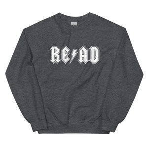 Puede incluir: Una sudadera gris oscuro con la palabra "READ" en blanco, estilizada para parecer un logotipo de banda de rock con un rayo.
