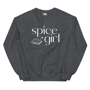 May include: A dark gray sweatshirt with the words "spice girl" in white script. A small open book graphic is below the words. The sweatshirt is a casual style.