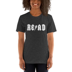 May include: A dark heather grey t-shirt with a white graphic of the word "READ" in a rock and roll font with a lightning bolt.
