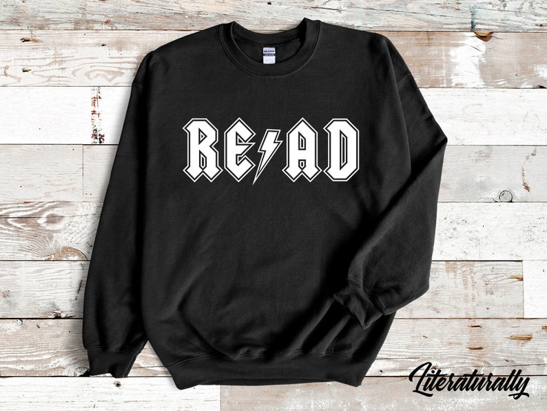 Puede incluir: Sudadera negra con un gr&aacute;fico blanco que dice "READ" en una fuente de estilo rock and roll con un rayo.
