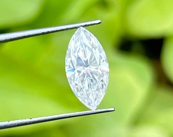 May include: A clear, faceted marquise-shaped diamond held by tweezers against a green background.