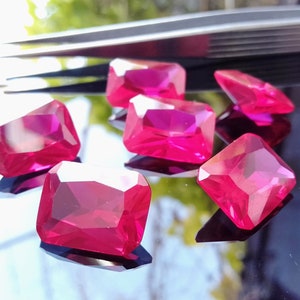Puede incluir: Seis piedras preciosas rectangulares facetadas de color rosa brillante sobre una superficie negra reflectante.