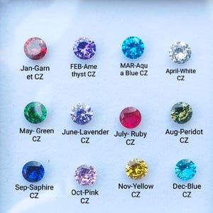 Puede incluir: Un gráfico que muestra doce piedras preciosas de diferentes colores, cada una representando un mes diferente del año. Las piedras preciosas están etiquetadas con el mes y el nombre de la piedra preciosa, como "Ene-Granate CZ" y "Feb-Amatista CZ".