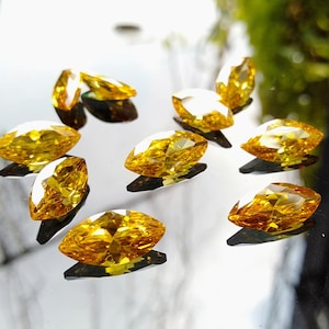 May include: A group of nine marquise-shaped, yellow gemstones on a reflective surface.