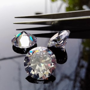 May include: Three clear round gemstones with a faceted design. The gemstones are on a black surface.