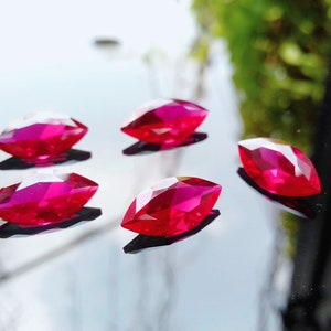 Pode incluir: Cinco pedras preciosas de forma marquesa de cor vermelha brilhante sobre uma superfície preta refletora.