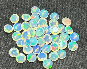May include: A collection of round, iridescent opal gemstones in various shades of white, blue, and green. The opals are faceted and have a smooth, polished finish.