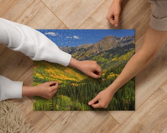 May include: Two people working together to complete a jigsaw puzzle of a mountain landscape with green trees and a blue sky.