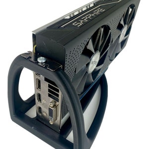 May include: A black graphics card with two fans and the text "SAPPHIRE" on the top. The card is mounted in a black plastic stand.
